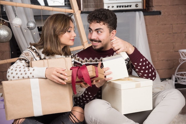 Young couple sitting on the floor with box gifts in Christmas interior.