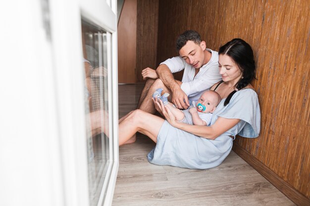 Young couple sitting on hardwood floor playing with their baby