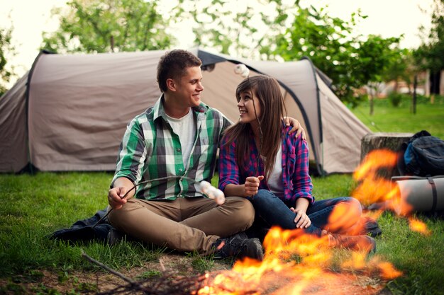 Young couple sitting near a campfire and toasting marshmallow