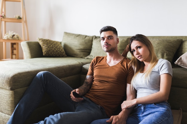自宅でテレビを見ているソファの近くに座っている若いカップル