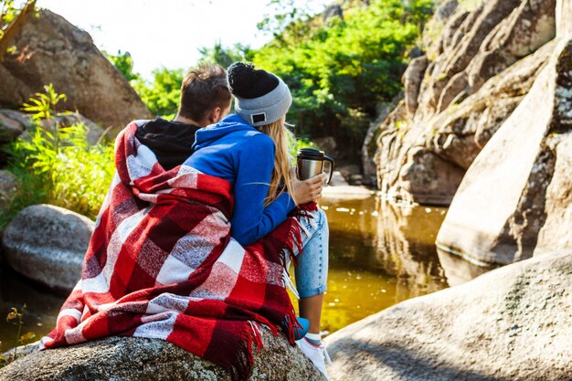 Young couple sitting on rock in canyon, drinking tea