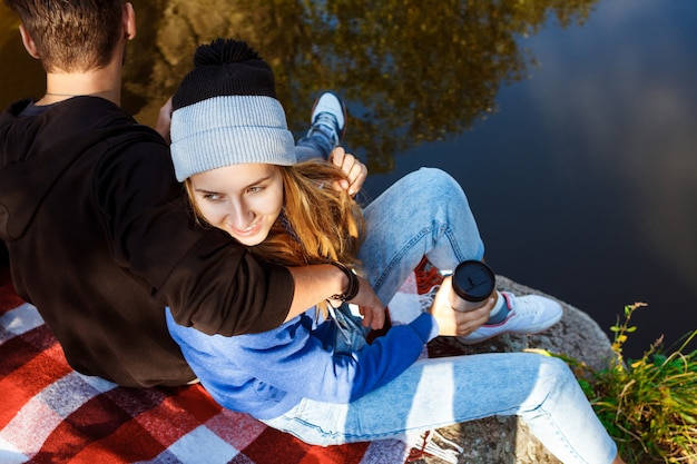 Young couple sitting on rock in canyon, smiling, drinking tea