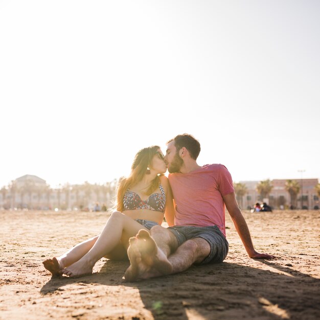 Young couple sitting on sandy beach kissing