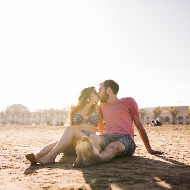 砂浜のビーチの上に座って若いカップルがキス