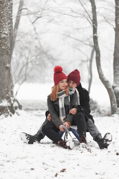 Молодая пара сидит на санях и играет со снегом