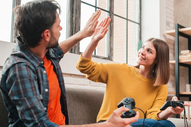 Free photo young couple sitting on sofa holding joystick giving high-five