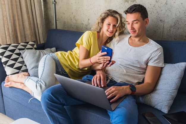 ノートパソコンで探している自宅のソファーに座っている若いカップル