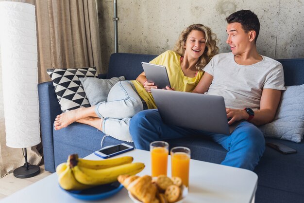 Молодая пара, сидя на диване у себя дома, глядя в ноутбук