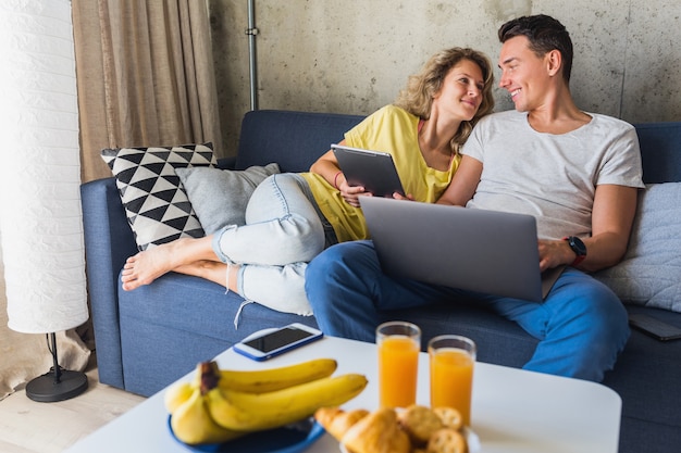 Young couple sitting on sofa at home looking in laptop