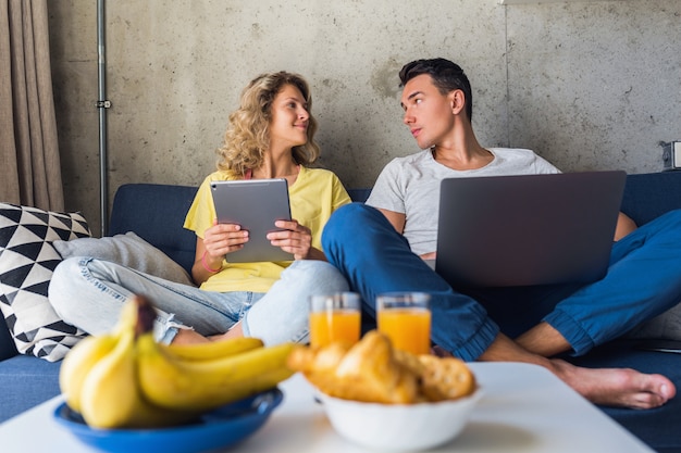 Young couple sitting on sofa at home looking in laptop