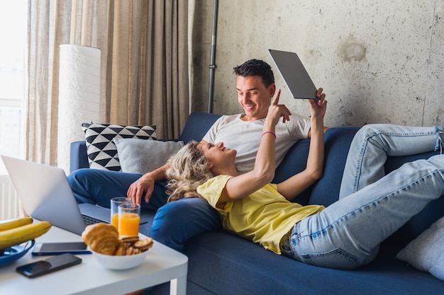 Young couple sitting on sofa at home looking in tablet, watching online