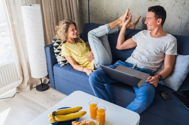 Young couple sitting on sofa at home using laptop