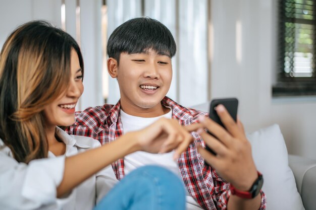 居間でソファに座って、一緒にゲームをプレイするスマートフォンを使用して、幸せな幸せな家族conceptx9で話したり笑ったりする若いカップル