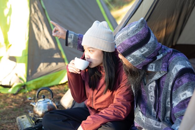 朝、テントに座ってコーヒーを飲む若いカップル