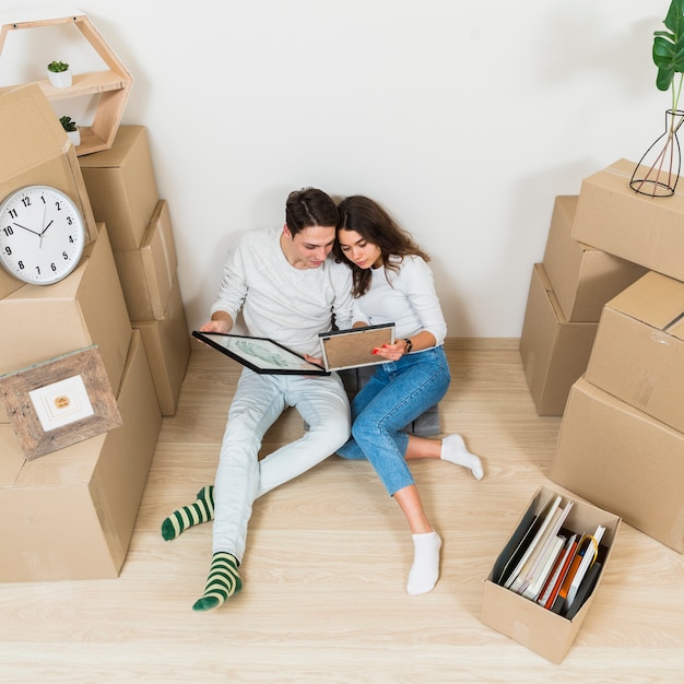 Free photo young couple sitting together looking at picture frame in their new apartment