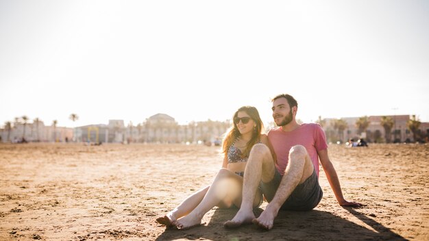 砂浜のビーチで一緒に座っている若いカップル