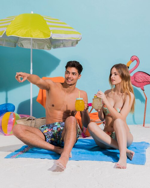 Young couple sitting on towel with cocktail in studio