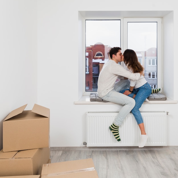 young couple sitting on window sill kissing each other in their new home