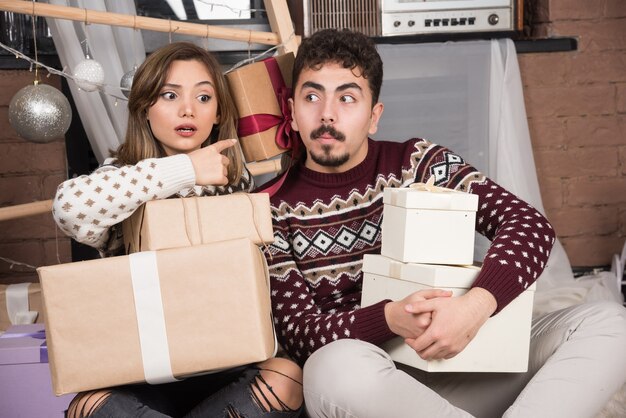 クリスマスと一緒に座っている若いカップルは、お祝いの銀のボールの近くにプレゼントします。
