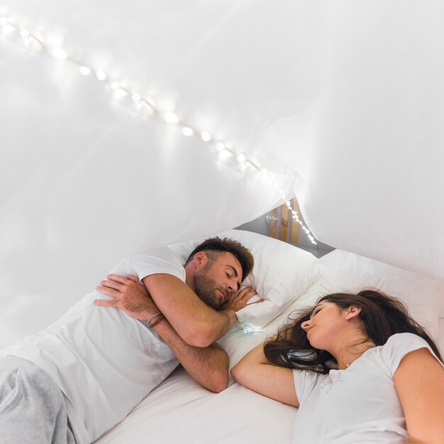 Young couple sleeping on bed under illuminated white cover
