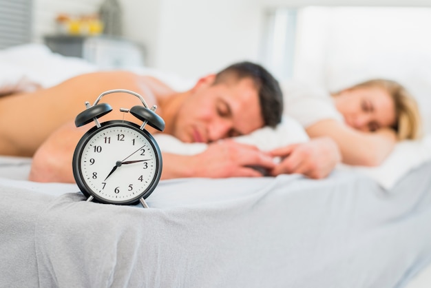 Young couple sleeping on bed near alarm clock 
