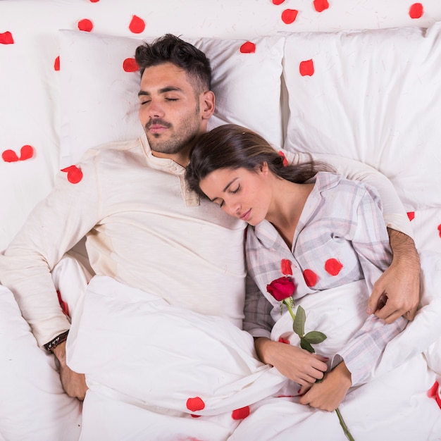 Free photo young couple sleeping in bed with red rose petals