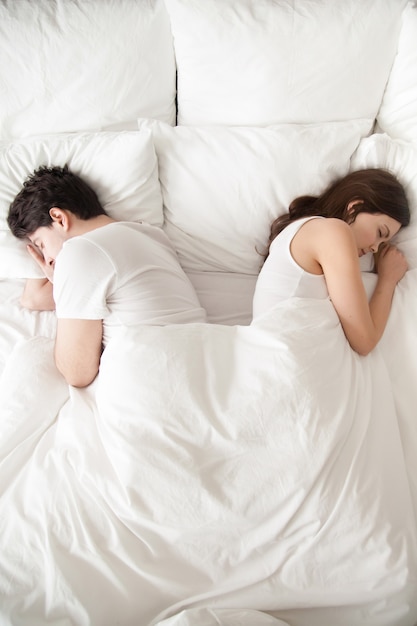 Young couple sleeping separately in bed, back to back, vertical