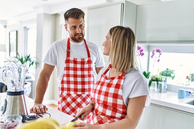 Free photo young couple smiling confident making smoothie cooking at kitchen