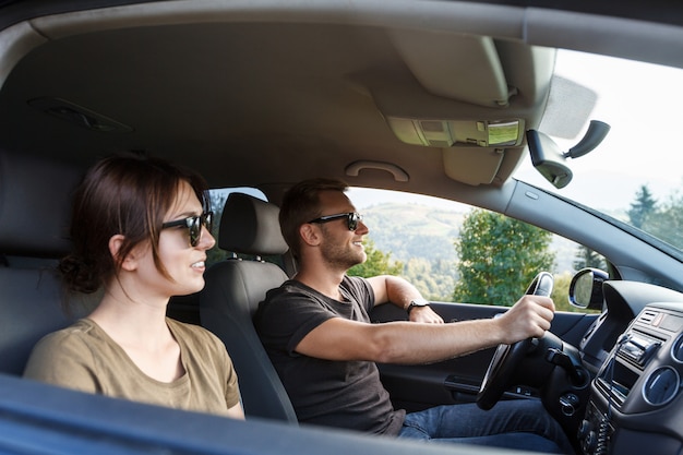 Young couple smiling, sitting in car, enjoying mountains view