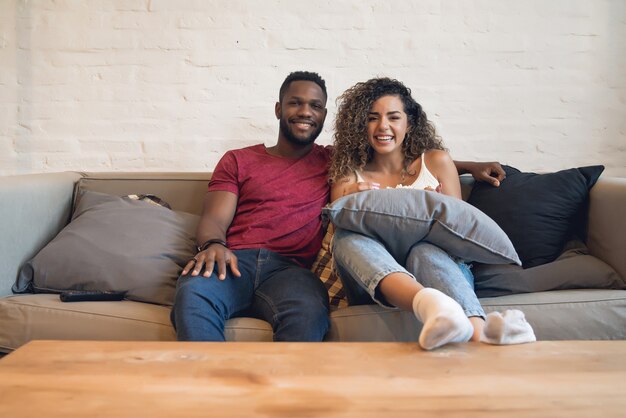 Young couple spending time together and watching tv series or movies while sitting on couch at home.