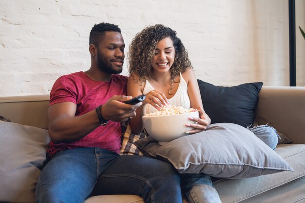 Young couple spending time together and watching tv series or movies while sitting on couch at home.