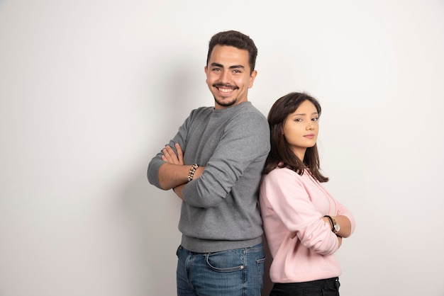 Young couple standing arms crossed on white.