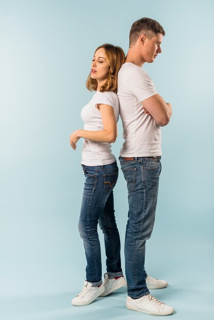 Young couple standing back to back against blue background