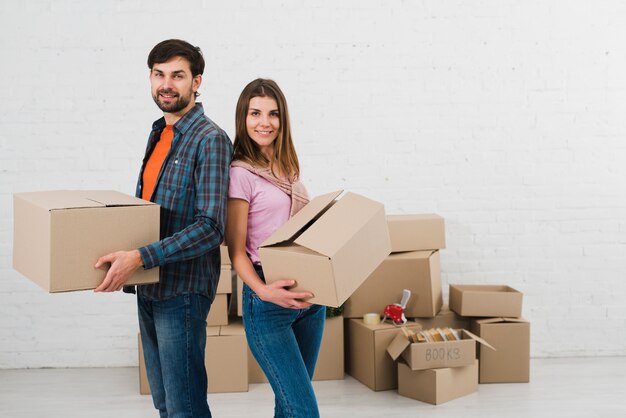 Young couple standing back to back holding cardboard boxes in hand