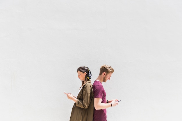 Free photo young couple standing back to back using cellphone