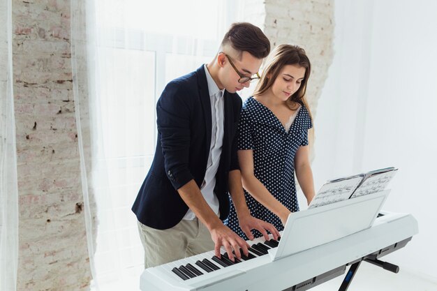 Young couple standing near the white curtain playing the piano