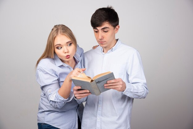 Free photo young couple standing and reading a book on gray wall