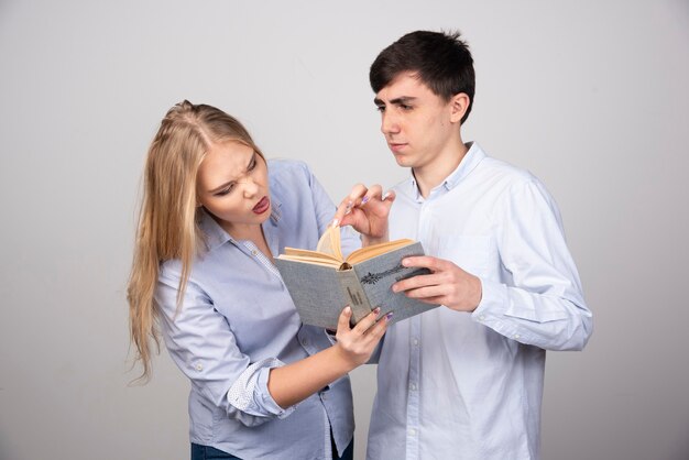 Young couple standing with book on gray background