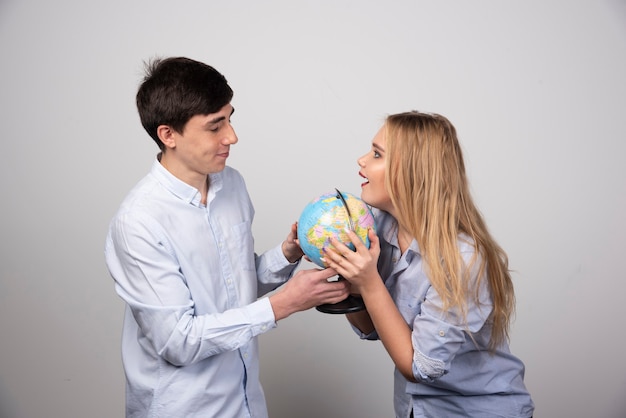 Young couple standing with an Earth globe on gray wall