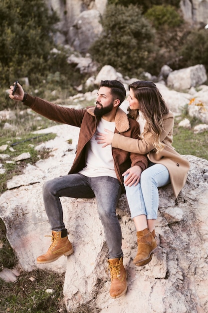 Young couple staying on a rock and taking a selfie