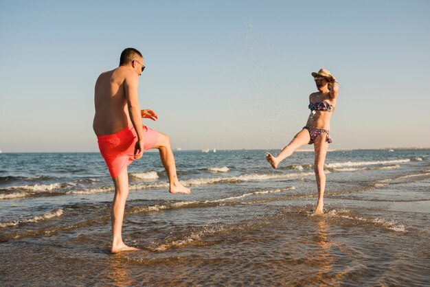Young couple in swimwear splashing the water at beach
