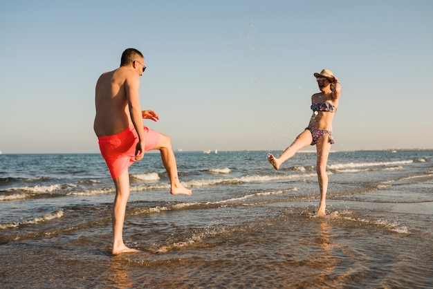 Young couple in swimwear splashing the water at beach