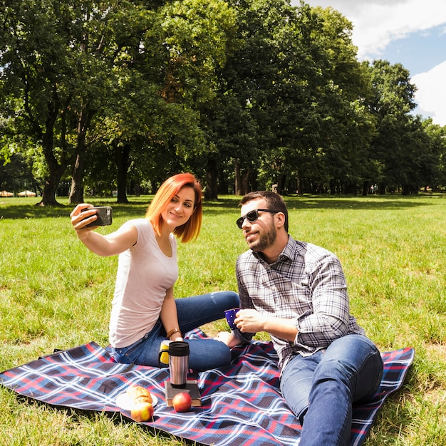 Молодая пара, занимая самоубийство на мобильном телефоне на открытом пикнике