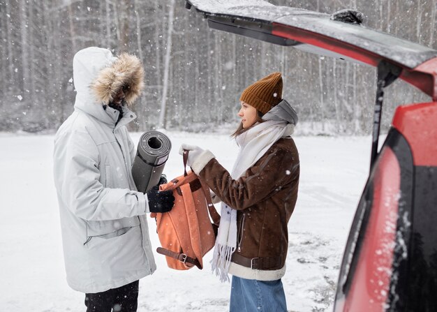 Молодая пара достает вещи из багажника автомобиля во время зимней поездки