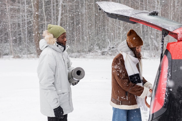 Young couple taking stuff out of car's trunk during a winter road trip