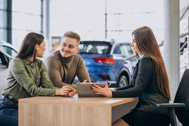 Young couple talking to a sales person in a car showroom