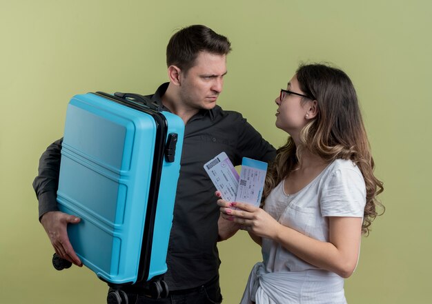 スーツケースと航空券を持ってお互いを見て不機嫌な光の壁の上に立っている観光客の男性と女性の若いカップル