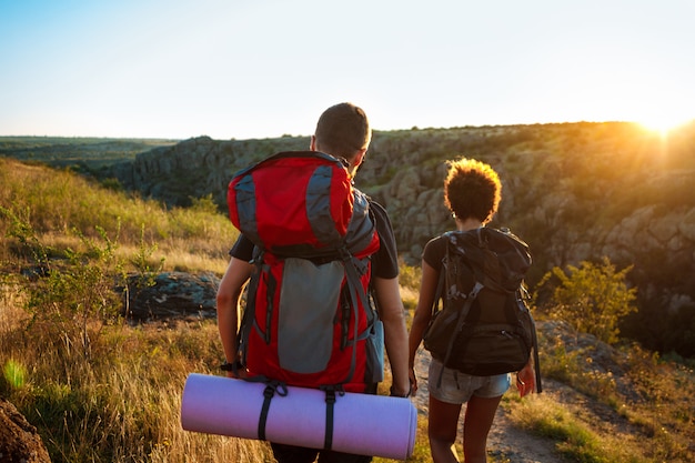 Young couple of travelers with backpacks traveling in canyon at sunset