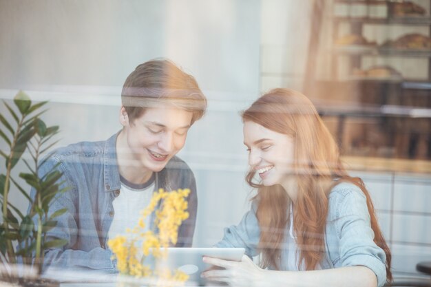 Young couple using smartphone behind glass