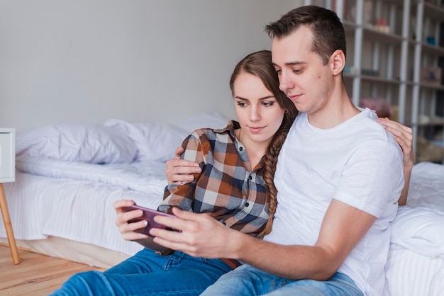 Young couple using smartphone near bed at home